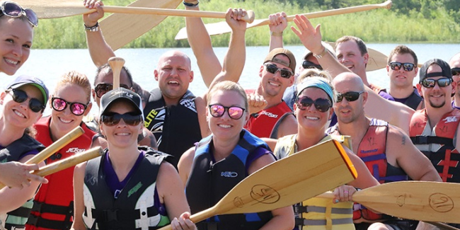 A dragon boat full of happy paddlers smiles and waves