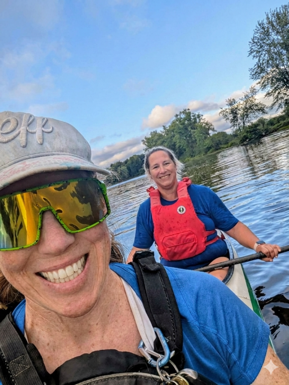 Two women smiling in a double sprint kayak on the river