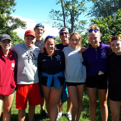 Eight coaches are smiling in the summer sun, with arms around each other.